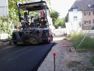 im Vordergrund frischer Asphalt. Asphaltmaschine steht vor der Kreuzung mit der Straße Im Defdahl.
