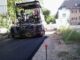 im Vordergrund frischer Asphalt. Asphaltmaschine steht vor der Kreuzung mit der Straße Im Defdahl.